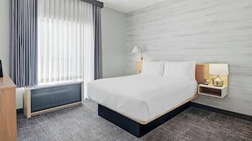 Ein Hotelzimmer mit einem Bett, einem Nachttisch mit Lampe, einem Fenster mit Vorhängen und einem Heizkörper.