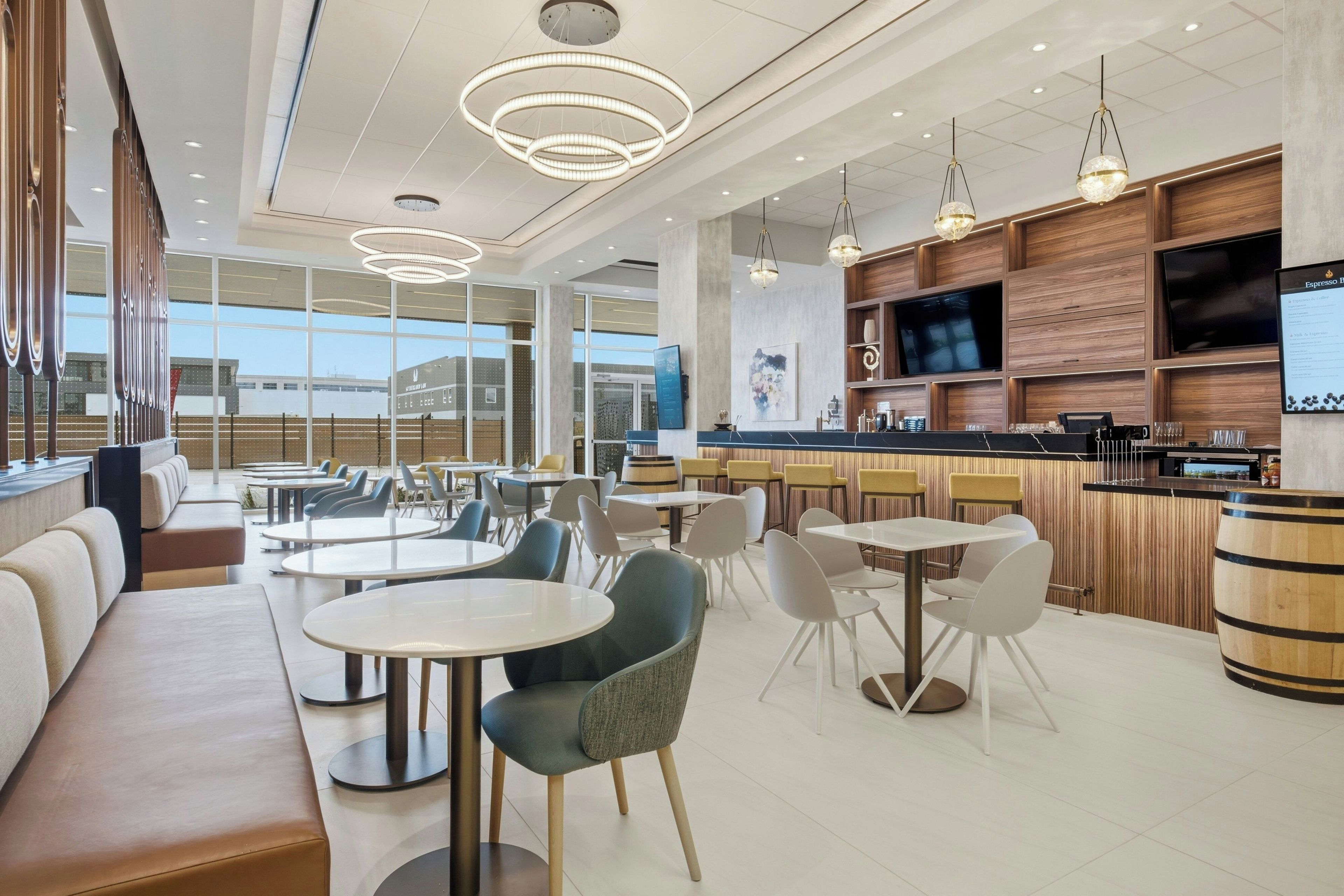 Una cafetería moderna con mesas y sillas redondas, y una zona de bar.