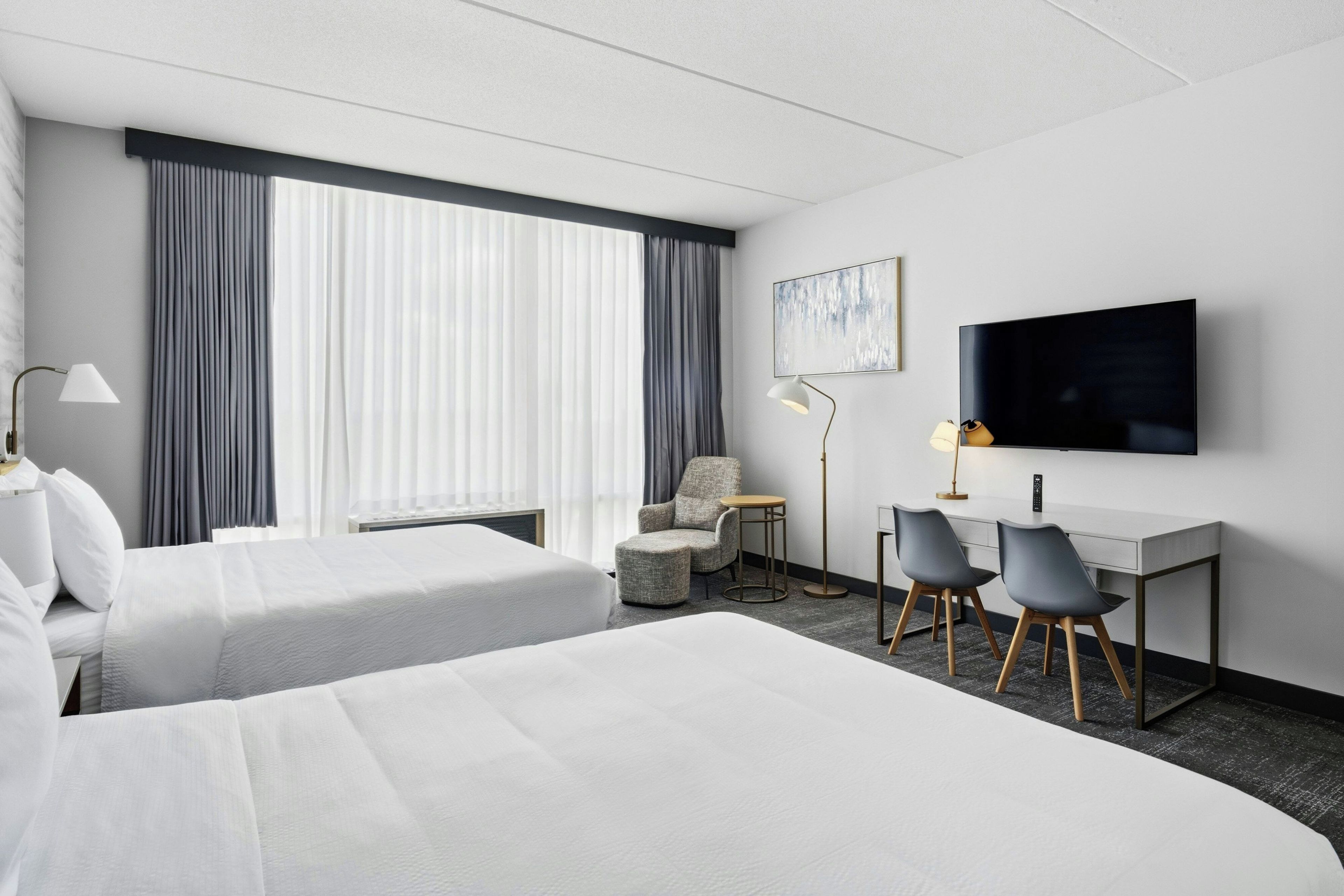 A hotel room with two beds, a desk with two chairs, a TV, and a window with curtains.