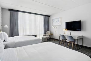 Habitación de hotel con dos camas, un escritorio con dos sillas, un televisor y una ventana con cortinas.