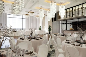 A banquet hall with round tables, white chairs, and chandeliers.