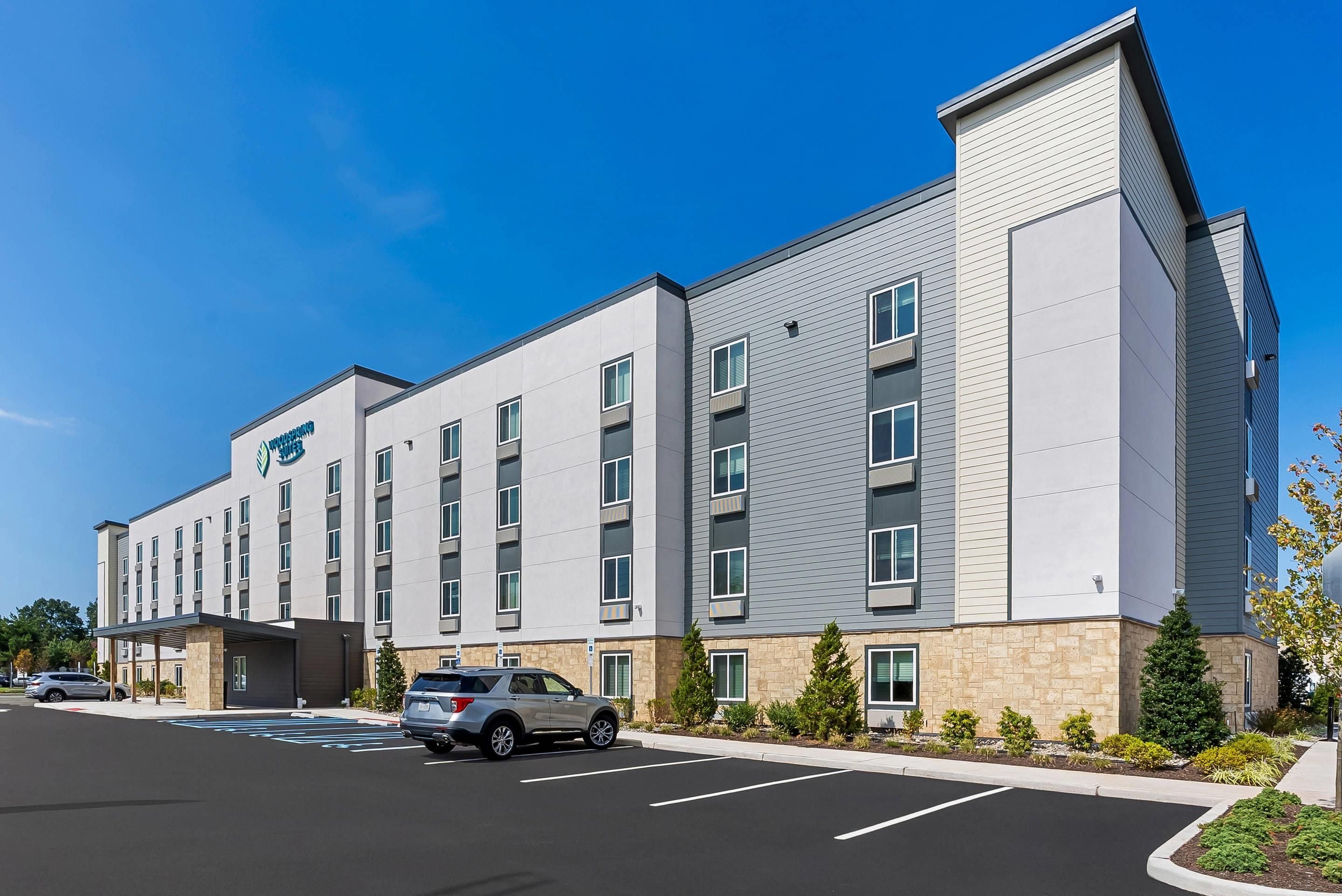 A modern hotel with a flat facade, multiple windows, and a parking lot with a few cars.
