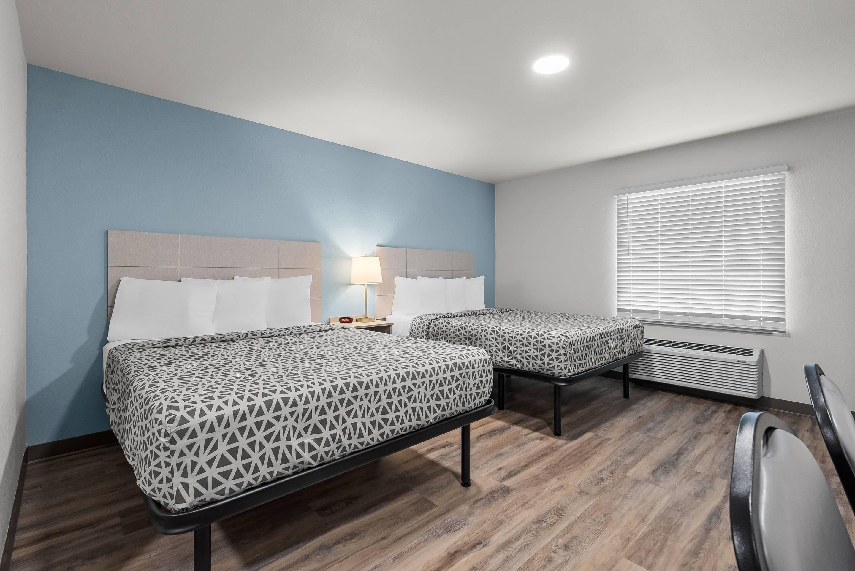 Een hotelkamer met twee bedden, een nachtkastje, een lamp, een raam met jaloezieën en een radiator.