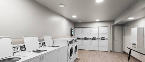 A laundry facility with multiple washing machines and dryers, a control panel, and a wooden floor.