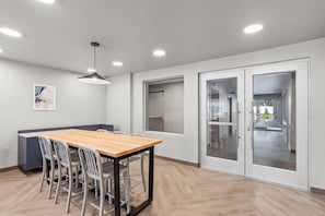 Un comedor moderno con una mesa de madera, sillas metálicas, luces empotradas en el techo y vistas a través de un ventanal.