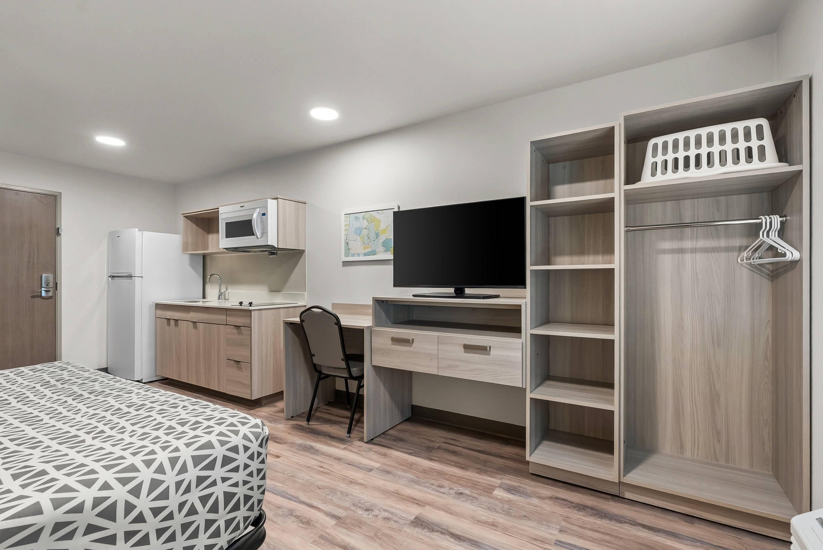 Un dormitorio moderno con cama, escritorio, televisor y armario.