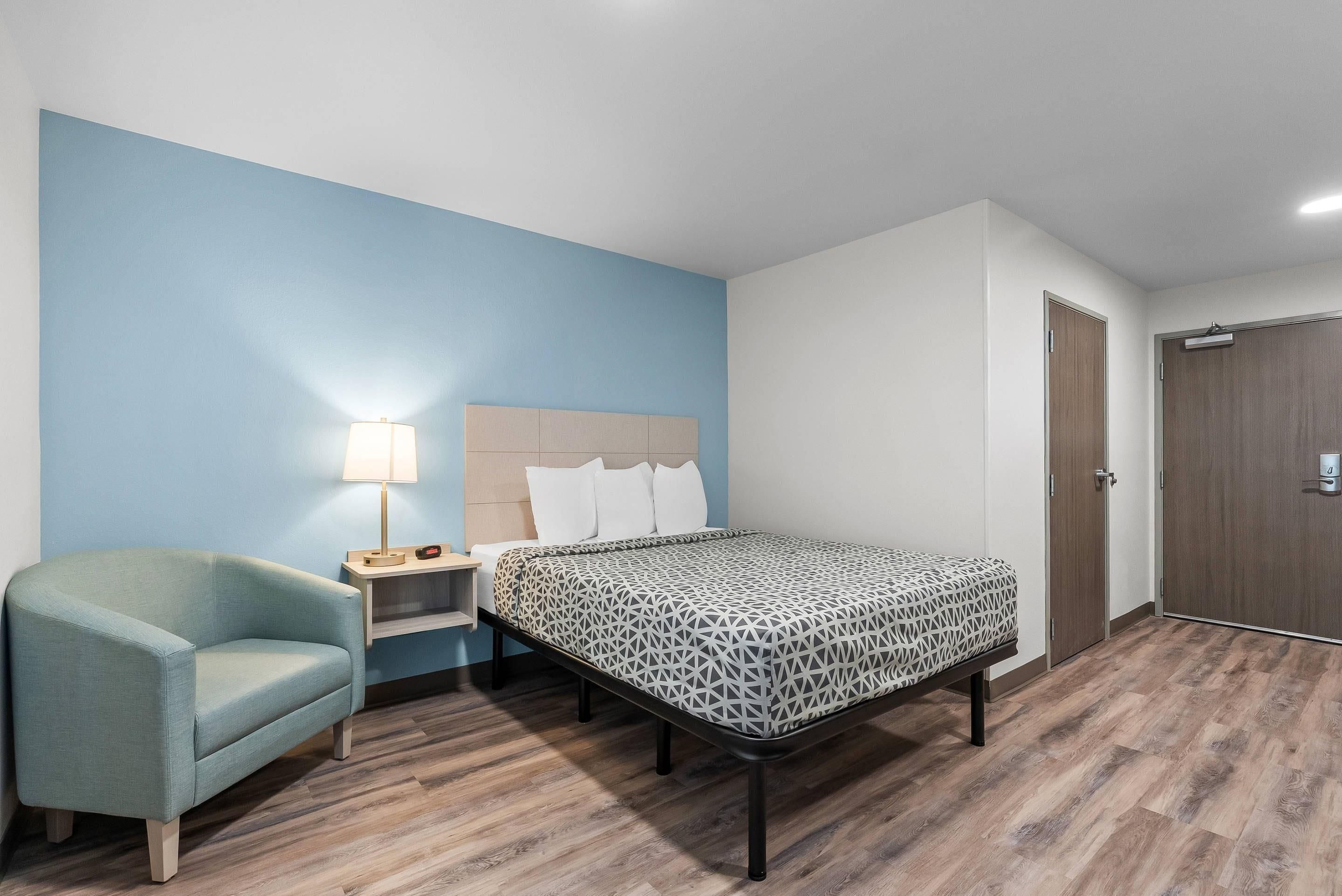 A hotel room with a bed, a chair, a nightstand, and a lamp.