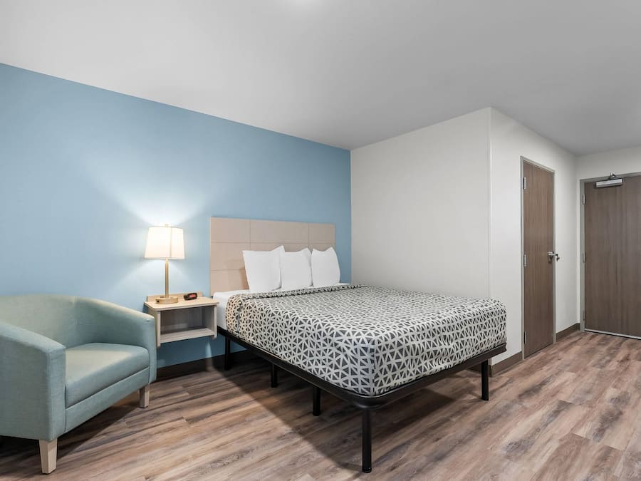 Una habitación de hotel con una cama, una silla, una mesita de noche y una lámpara.