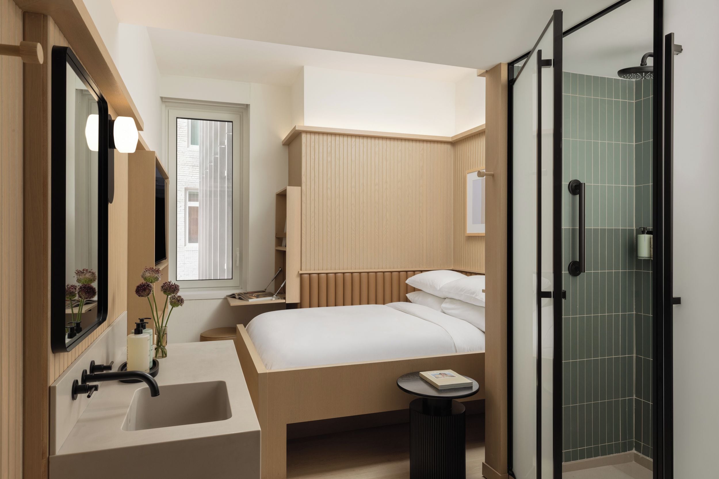 A modern bathroom with a large mirror, a sink, a shower, and a bed with a bedside table.