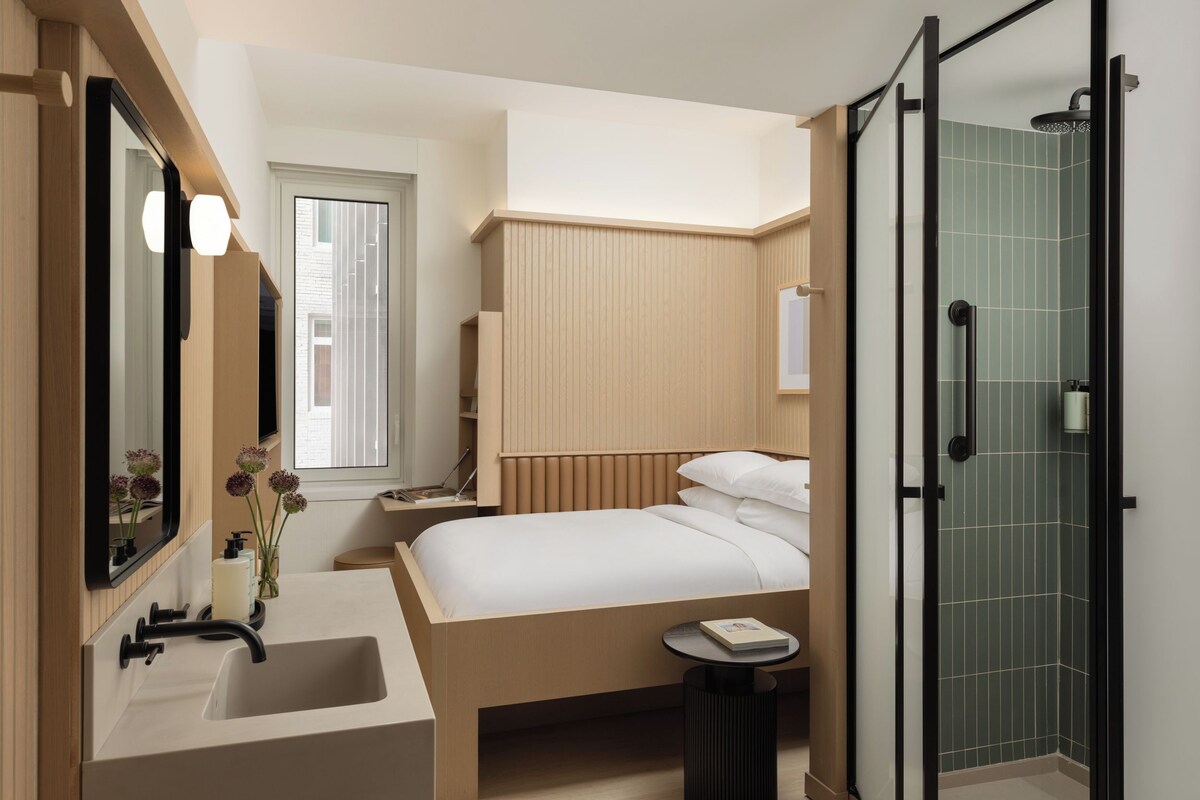 Un baño moderno con un espejo grande, un lavabo, una ducha y una cama con mesita de noche.