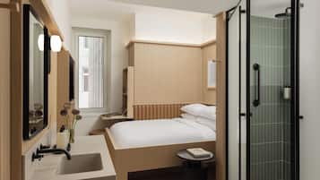 A modern bathroom with a large mirror, a sink, a shower, and a bed with a bedside table.