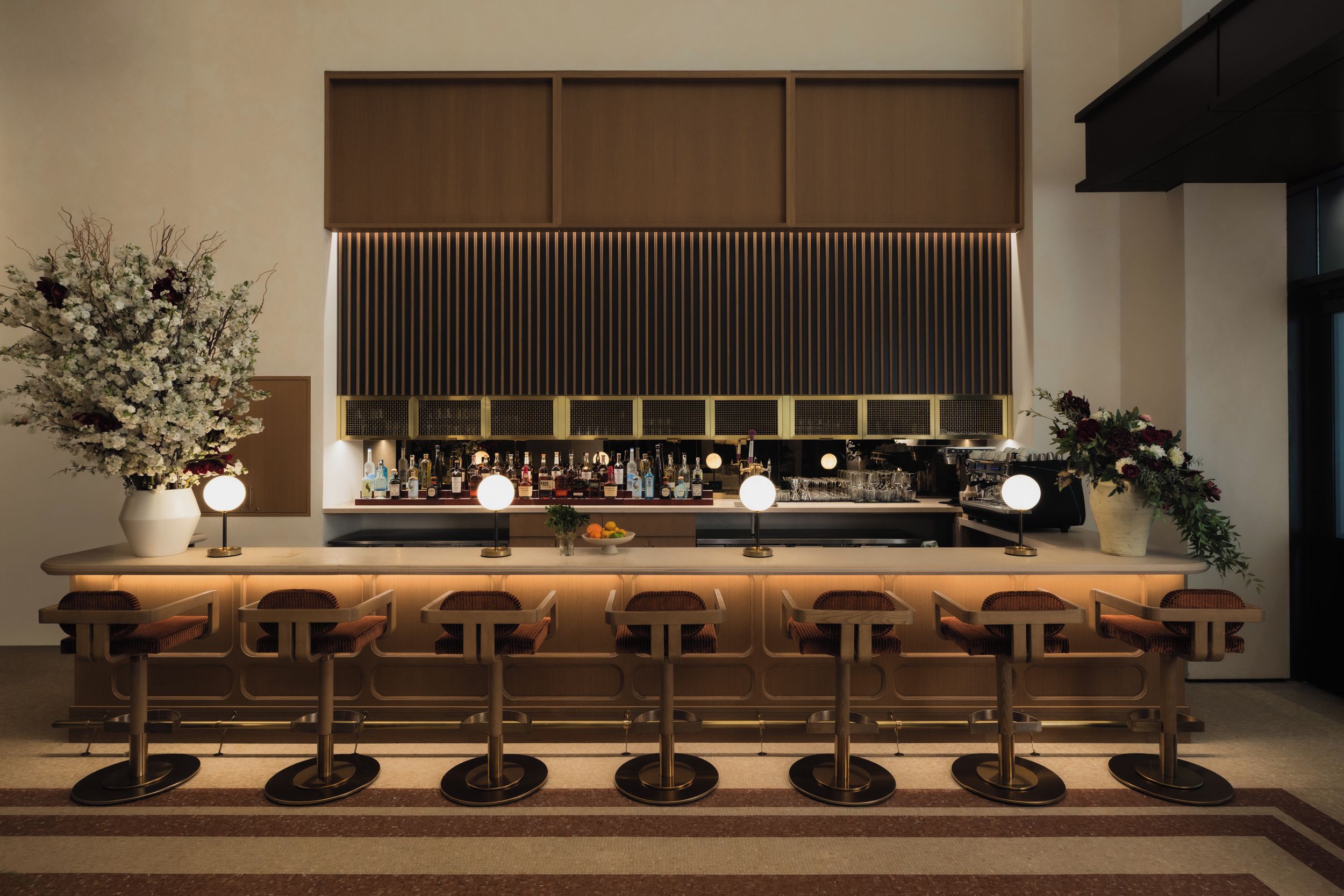 Een bar met een lange toonbank, meerdere stoelen en een divers assortiment flessen en glazen.