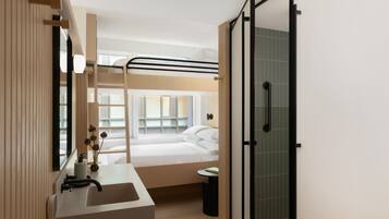 A modern hotel room with a bunk bed, a bathroom with a sink and mirror, and a glass shower enclosure.