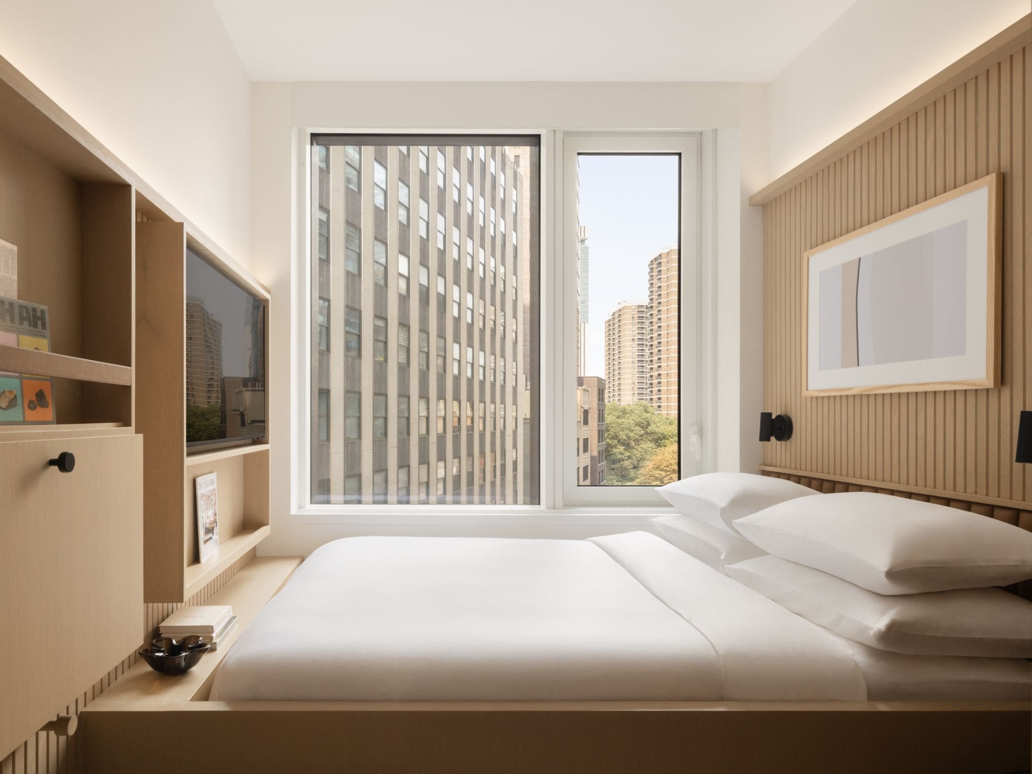 A modern bedroom with a large bed, a window with blinds, a television on a stand, and a framed picture on the wall.