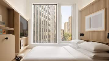 A modern bedroom with a large bed, a window with blinds, a television on a stand, and a framed picture on the wall.