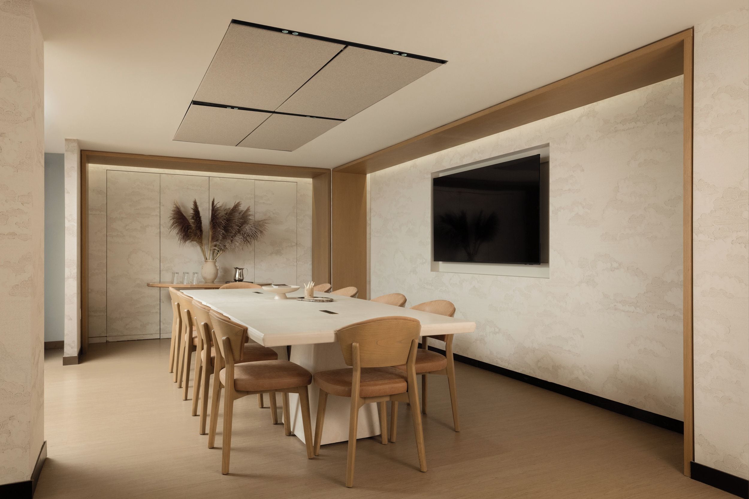 A conference room with a long table, chairs, a vase with pampas grass, and a television on the wall.