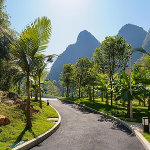 A curved road with a grassy median, surrounded by tropical vegetation and mountains in the background. - TUI Blue Yangshuo Xiangheli Hotel (GUILIN)