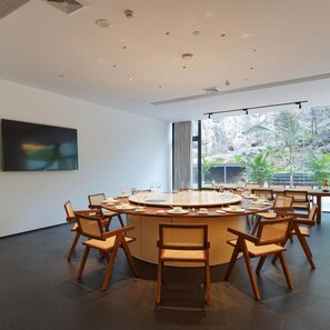 A conference room with a round table, chairs, and a large window with a view of greenery. - TUI Blue Yangshuo Xiangheli Hotel (GUILIN)