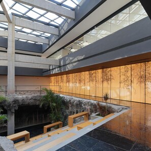 Un interior moderno con una fuente central, bancos de madera y un techo de cristal.