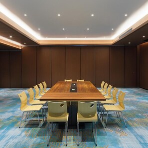 Un salón de conferencias con una larga mesa y varias sillas, alfombra estampada e iluminación empotrada en el techo.