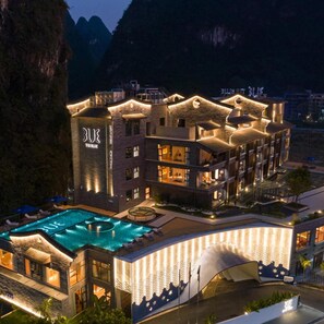 A multi-story hotel with a swimming pool, a large entrance canopy, and a mountainous backdrop. - TUI Blue Yangshuo Xiangheli Hotel (GUILIN)