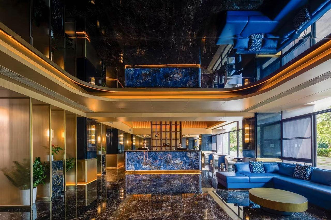 Un moderno vestíbulo de hotel con un mostrador de recepción de mármol, área de descanso y ventanas amplias.