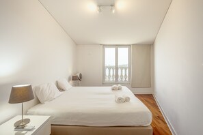 Une chambre d’hôtel avec un lit, une table de chevet avec une lampe, un ventilateur et une fenêtre donnant sur un balcon.