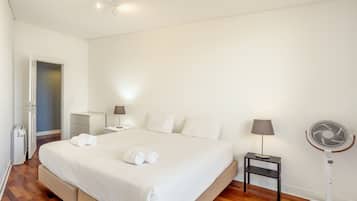 Een hotelkamer met een bed, nachtkastjes, een lamp, een ventilator en een deur.