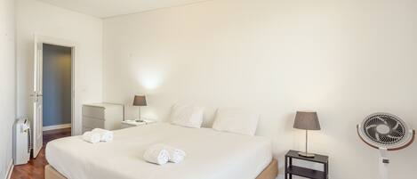 Une chambre d’hôtel avec un lit, des tables de chevet, une lampe, un ventilateur et une porte.