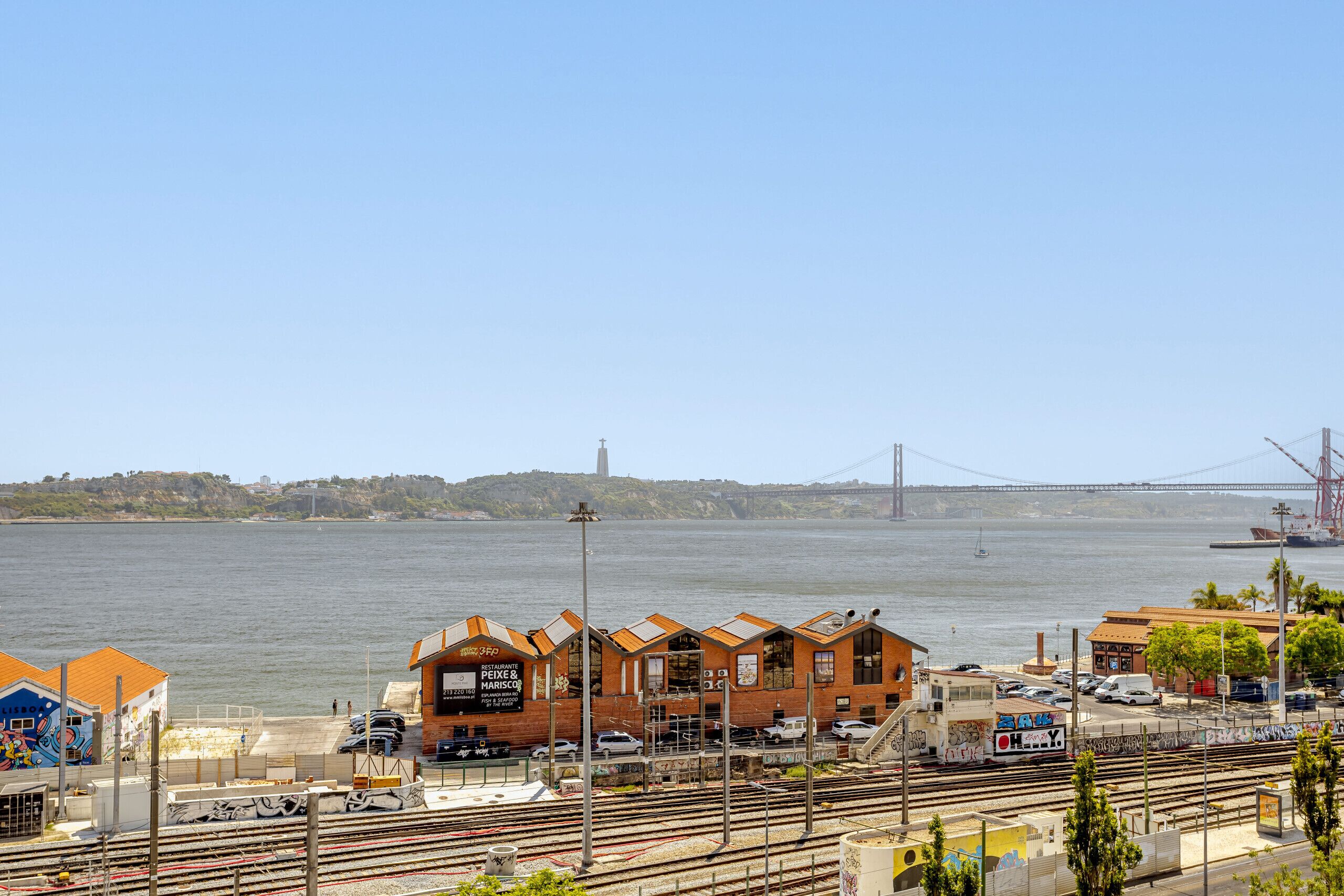 A waterfront property with a restaurant named 'Peixe & Marisco' and a view of the river and a bridge in the background.