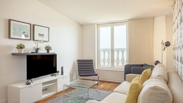 Een moderne woonkamer met een flatscreen televisie, een glazen salontafel, een bank en een fauteuil.