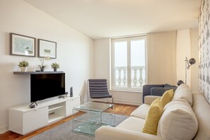 A modern living room with a flat-screen TV, a glass coffee table, a sofa, and a chair. - Downtown Riverside V by Homing (Lisbon)