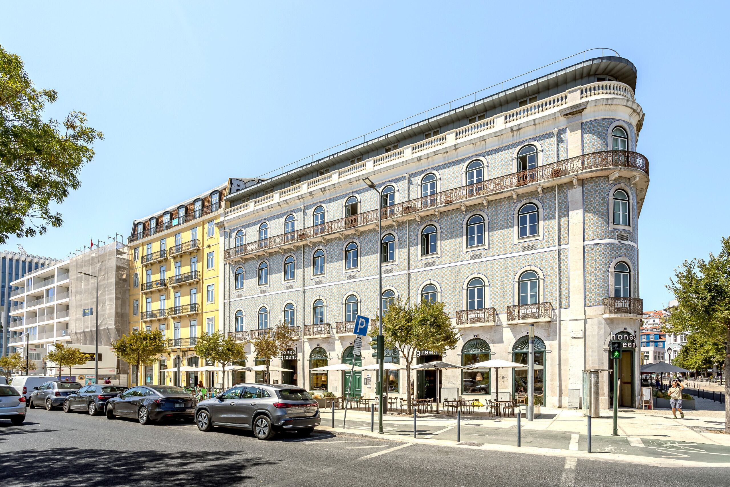 A multi-story building with a curved facade, multiple balconies, and a ground-level cafe.