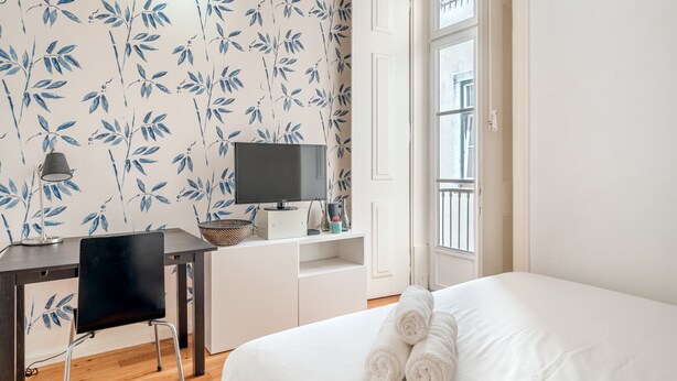 A bedroom with a bed, a desk with a TV, a chair, and a window with a view. - Downtown Riverside IV by Homing (Lisbon)