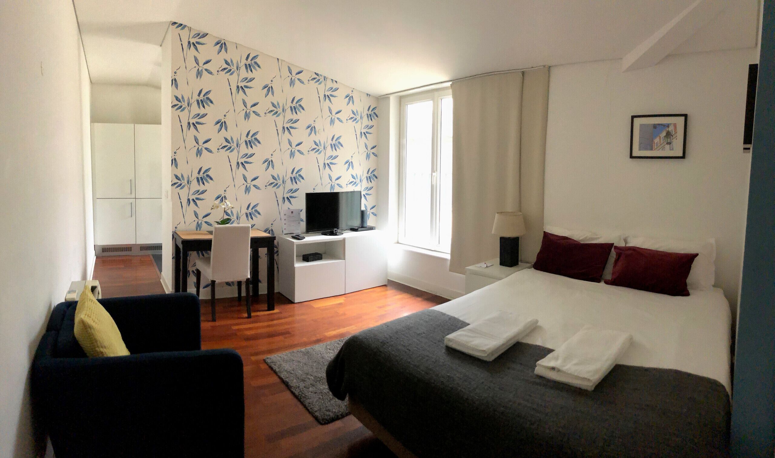 A hotel room with a bed, a desk with a computer, a chair, and a window.