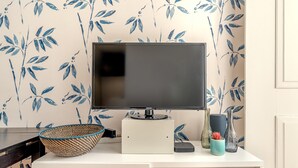 A flat-screen TV on a white stand, a woven basket, and decorative vases on a white desk against a wall with a blue leaf pattern. - Downtown Riverside IV by Homing (Lisbon)