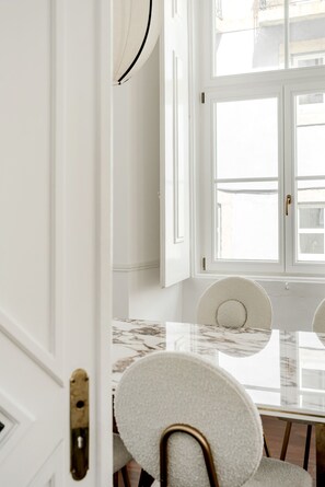 A room with a white door, a glass table, and a chair with a white cushion. - Chiado Deluxe by Homing (Lisbon)
