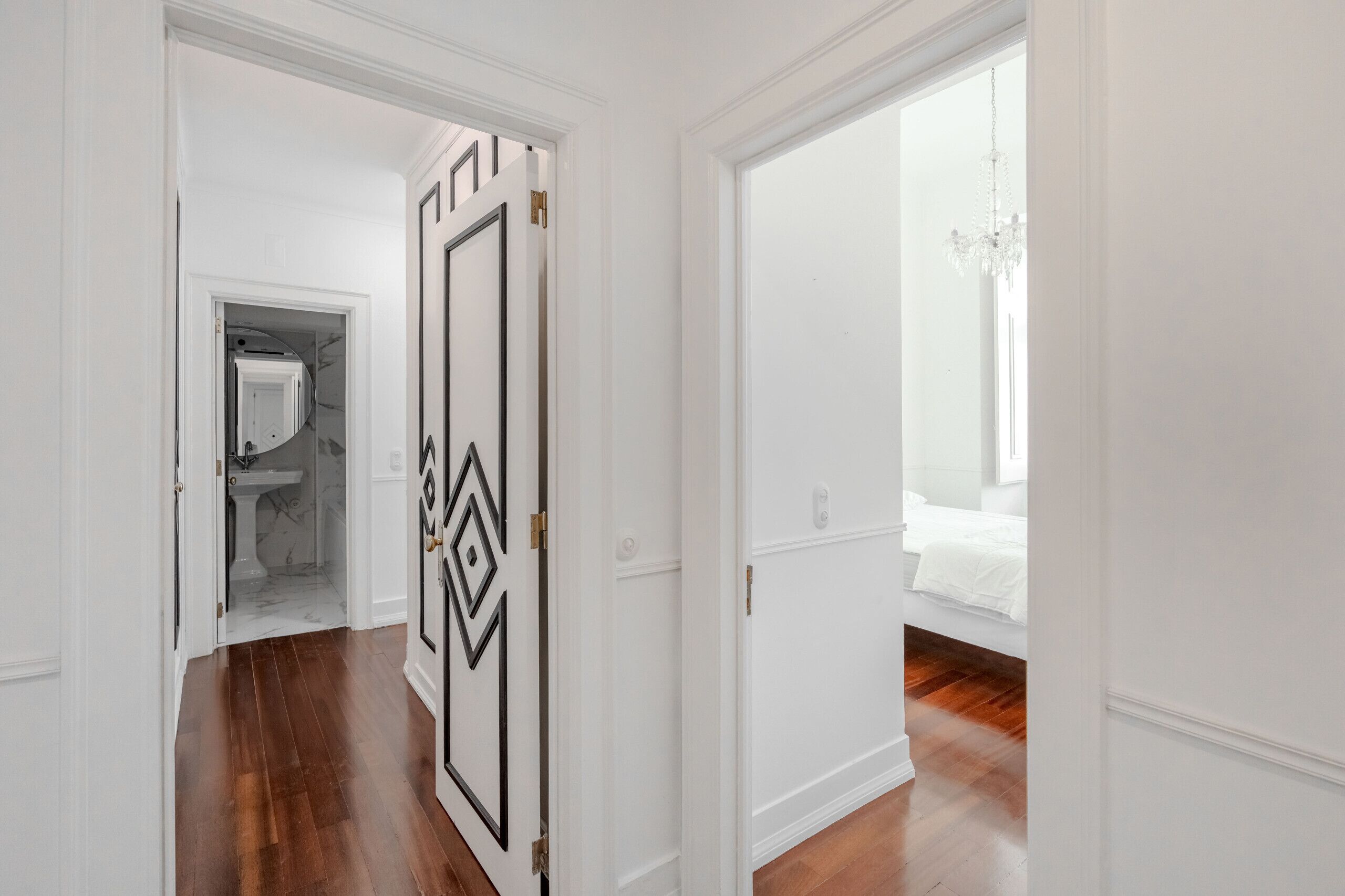 A hallway with a door leading to a bedroom with a bed and a chandelier.