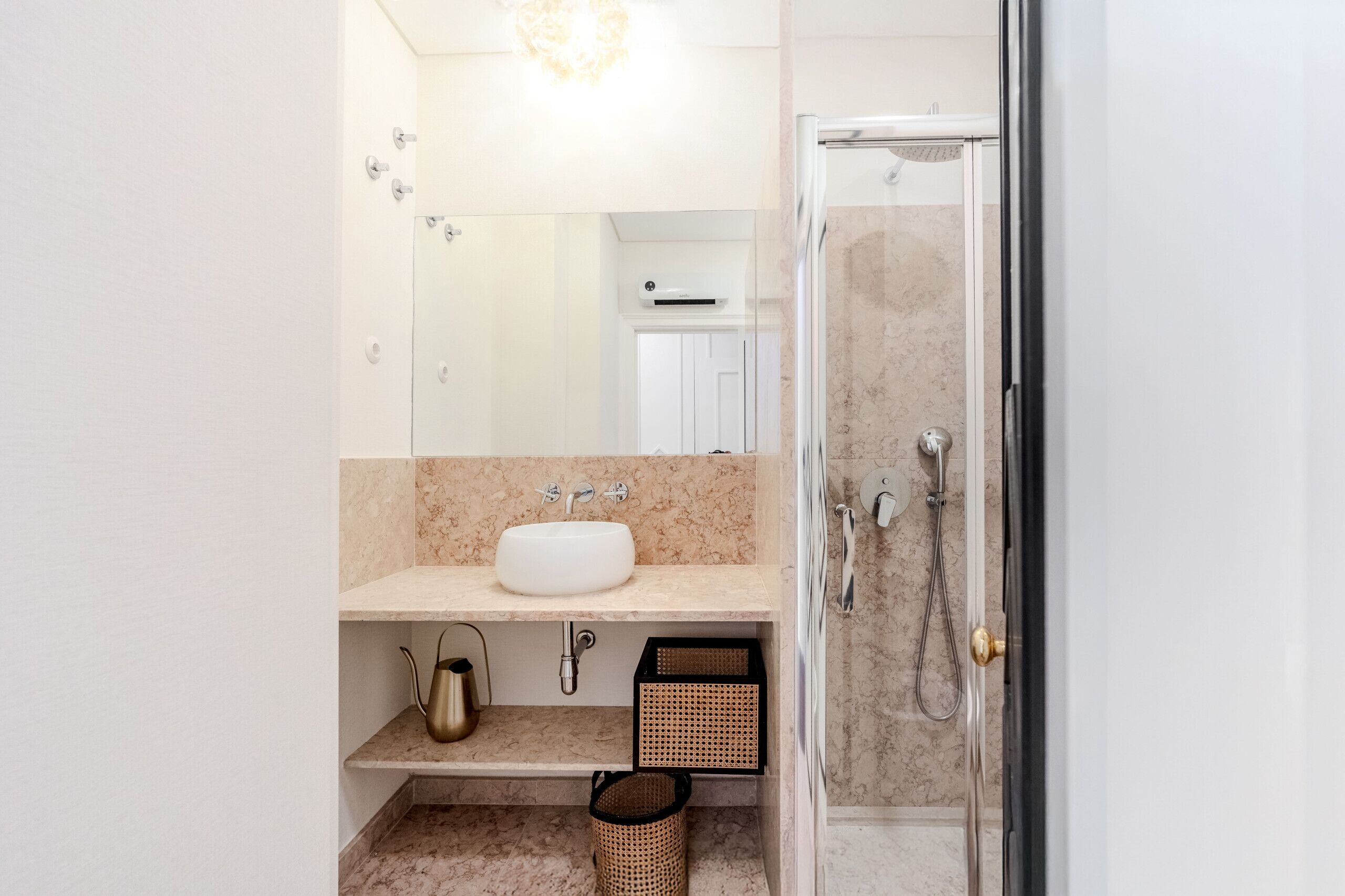 Un baño con lavamanos, espejo, ducha y toallero.