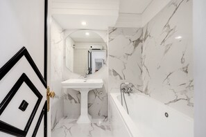 A bathroom with a pedestal sink, a bathtub, and a marble wall. - Chiado Deluxe by Homing (Lisbon)