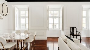 A spacious room with a marble dining table, white upholstered chairs, a beige sofa, and a dark wooden chair. - Chiado Deluxe by Homing (Lisbon)