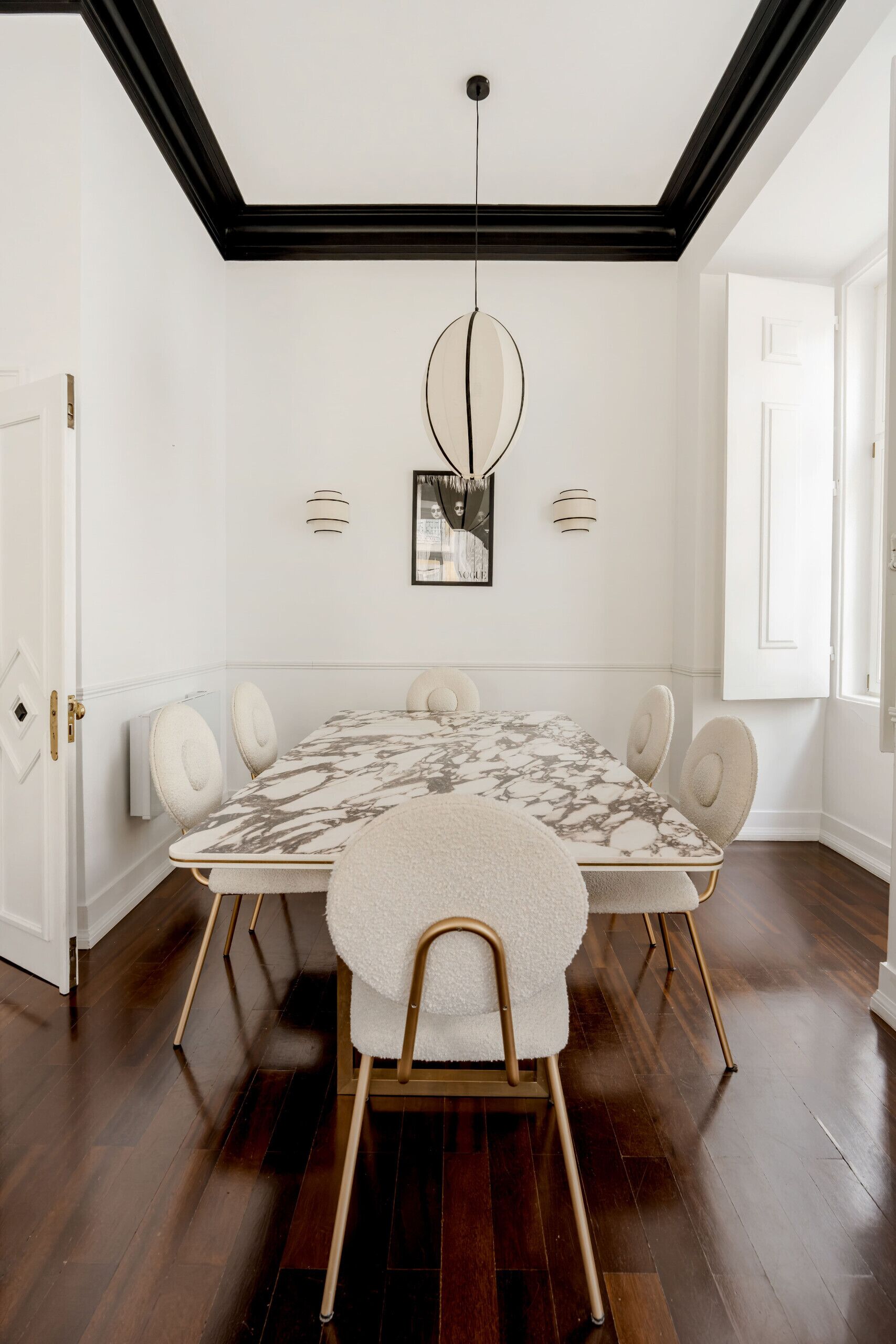 A dining room with a marble table, white chairs, a chandelier, and a white door.