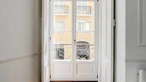 A hallway with wooden flooring, a white door, and a view of a yellow building with balconies. - Chiado Deluxe by Homing (Lisbon)