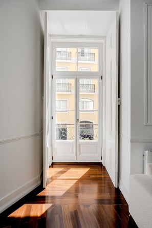 Ein Flur mit Holzboden, einer weißen Tür und Blick auf ein gelbes Gebäude mit Balkonen.