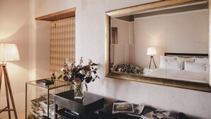 A hotel room with a bed, a large mirror, a bedside table with a lamp, a vase with flowers, and a bookshelf. - Ma' Ca' - New York (Praiano)