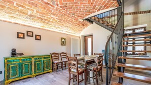 Uma sala de jantar com teto de tijolos, cadeiras de madeira, um armário verde e uma escadaria.