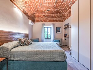 A bedroom with a brick ceiling, a bed with patterned pillows, a window with a view, and a small seating area. - Casa Vescovo by Interhome (Asti)
