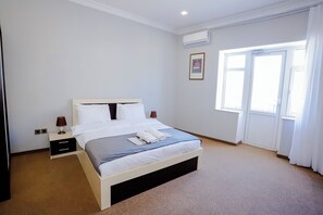 A bedroom with a bed, bedside tables, an air conditioning unit, a window, and a door. - Kichik Gala 98 (Baku)