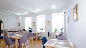 A dining area with wooden tables and chairs, a kitchen in the background, and framed pictures on the walls. - Kichik Gala 98 (Baku)