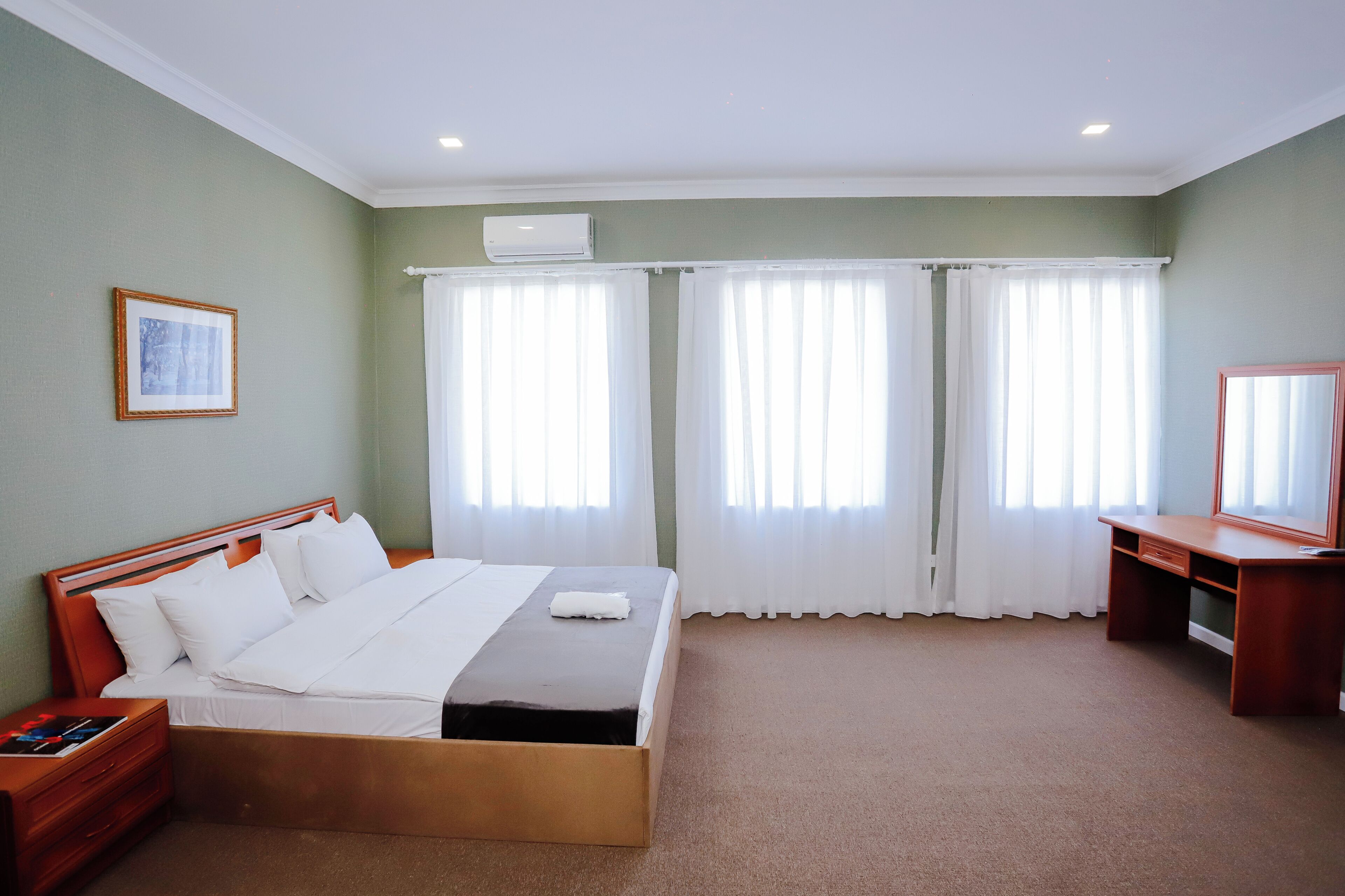 Quarto de hotel com cama, escrivaninha, cadeira e janela com cortinas.